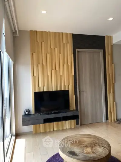 Modern living room with stylish wooden paneling and mounted TV, featuring a round wooden coffee table.