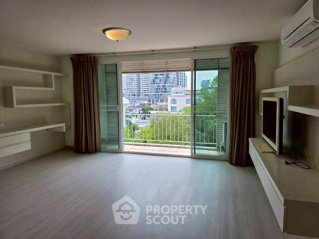Spacious living room with balcony and city view, featuring modern built-in shelves and air conditioning.
