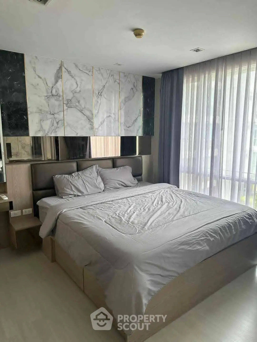 Modern bedroom with stylish marble accent wall and large windows for natural light.