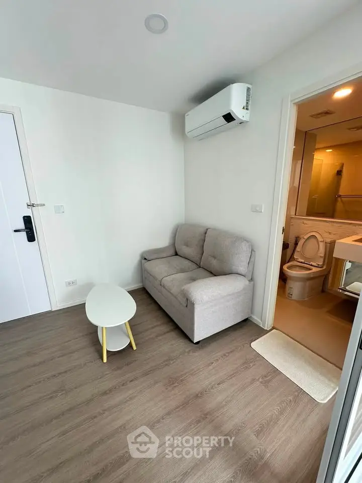 Cozy living room with modern sofa and air conditioning, adjacent to a compact bathroom.