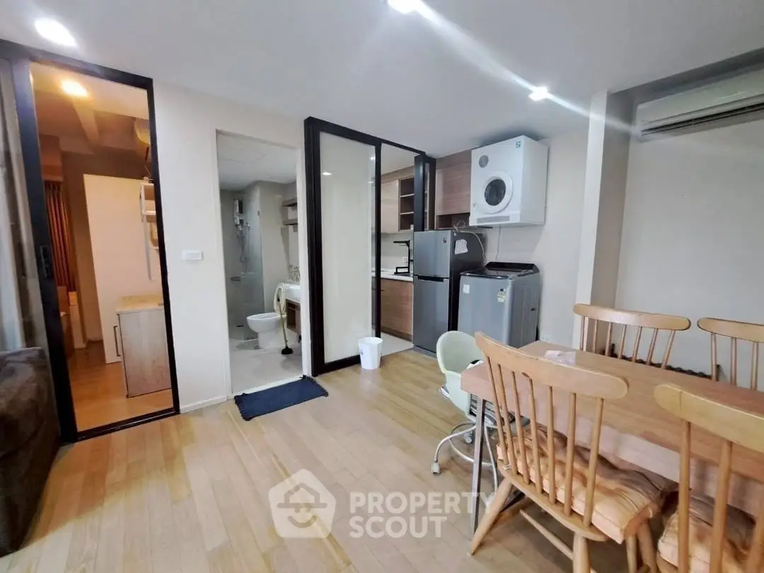 Modern open-plan living space with dining area, kitchen, and laundry appliances in a cozy apartment.