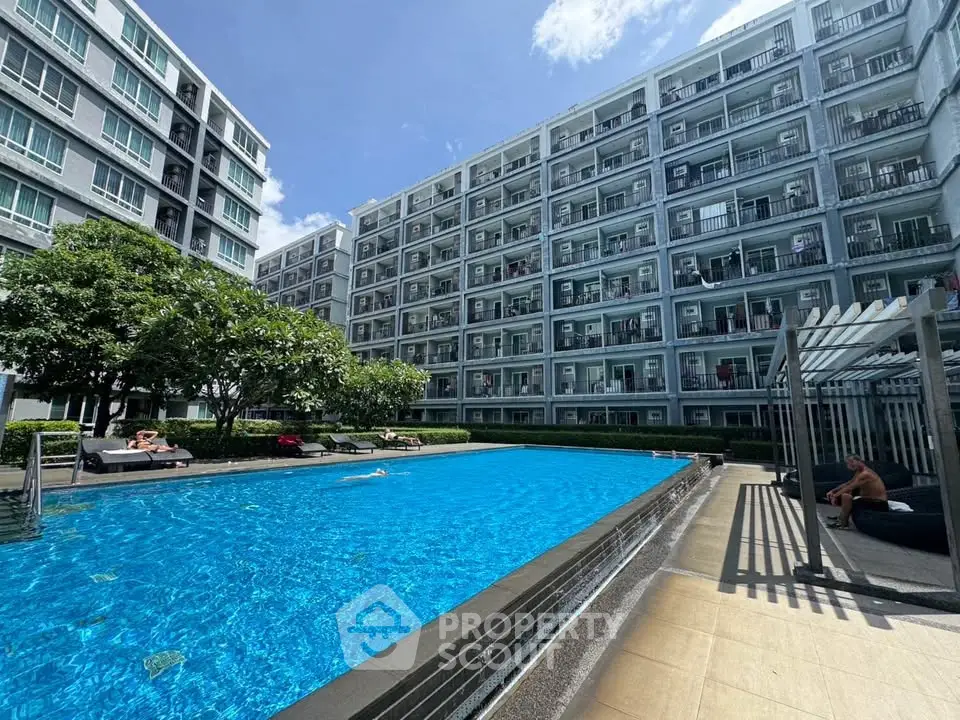 Modern apartment complex with a large swimming pool and sunbathing area under a clear blue sky.