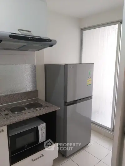 Compact kitchen with modern appliances including fridge and microwave in a cozy apartment.