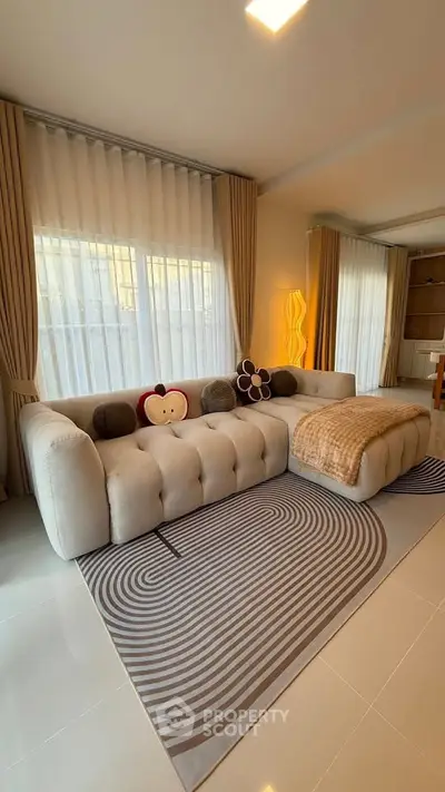 Spacious living room with modern sofa and stylish decor, featuring large windows and elegant curtains.