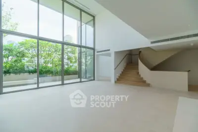 Spacious modern living room with large windows and garden view, featuring elegant staircase.