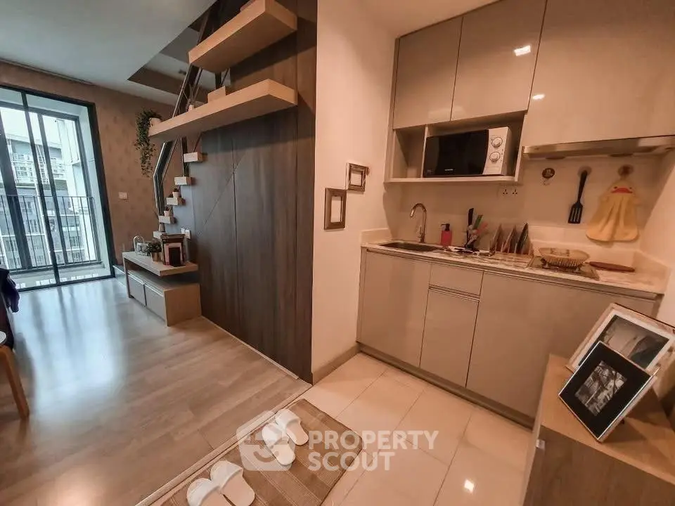 Modern open-plan living room with stylish kitchen and staircase, featuring sleek cabinetry and natural light.