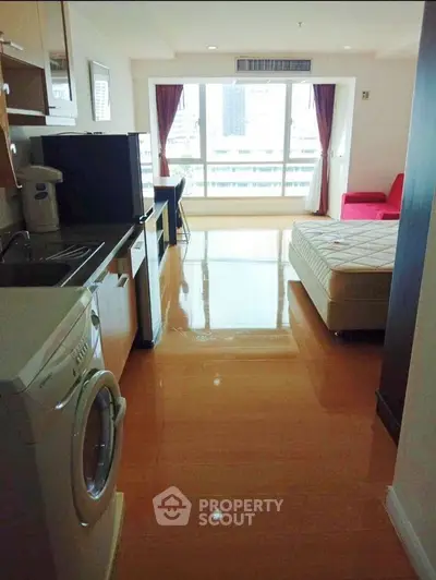 Modern studio apartment with open layout, featuring a washing machine and city view from large windows.