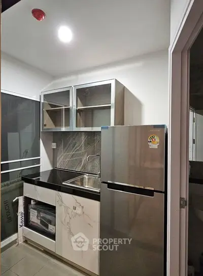 Modern kitchen with sleek design, featuring stainless steel fridge and marble countertops.