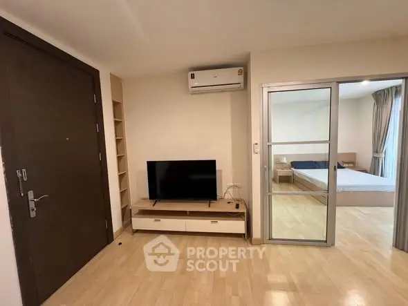 Modern apartment interior with TV and bedroom view, featuring sleek wooden flooring and air conditioning.