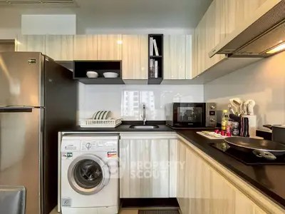 Modern kitchen with sleek cabinetry, washing machine, and stainless steel appliances in a stylish apartment.