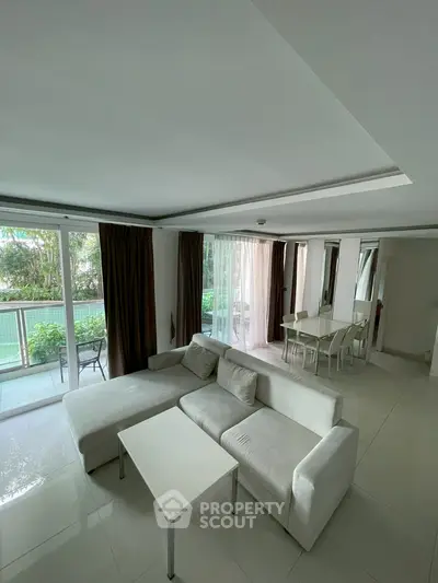 Spacious living room with modern white sofa and dining area, featuring large windows and garden view.