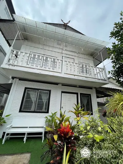 Charming two-story white house with balcony and lush garden