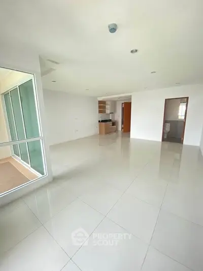 Spacious open-plan living room with modern kitchen and large windows in a bright apartment.