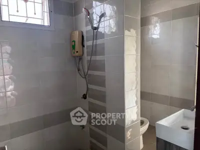 Modern bathroom with sleek tiles and compact design, featuring a shower and sink.