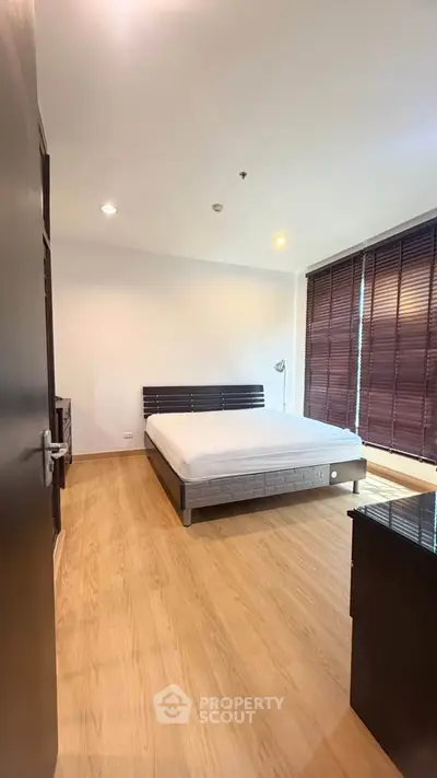 Spacious bedroom with wooden flooring and large windows in modern apartment.