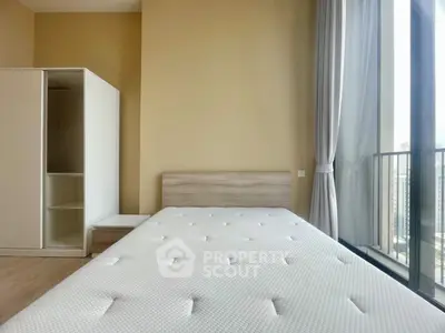 Spacious bedroom with large window and modern furnishings in a high-rise apartment.