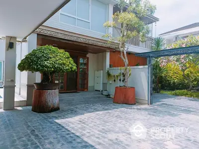 Spacious modern home entrance with lush greenery and paved driveway