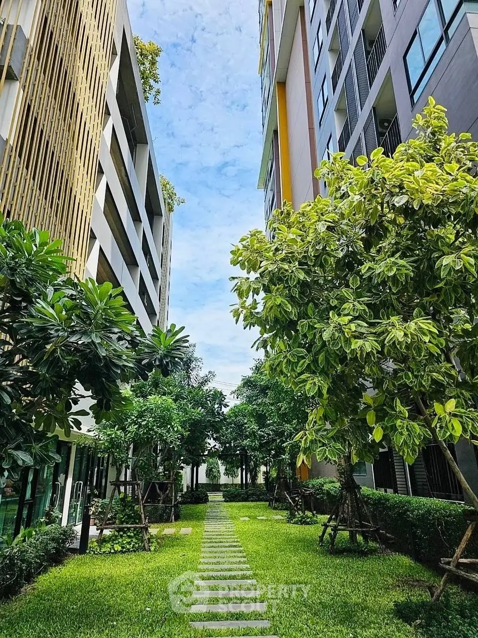 Lush garden pathway between modern apartment buildings with vibrant greenery.