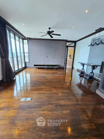 Spacious living room with wooden flooring and large windows offering natural light