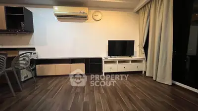 Spacious living room with modern decor and wooden flooring, featuring a TV and air conditioning.
