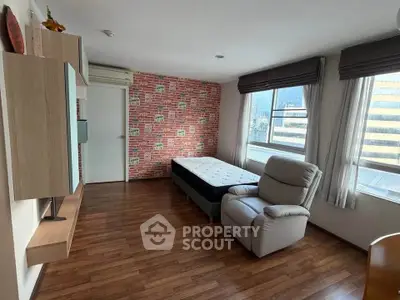 Modern bedroom with city view, featuring stylish brick accent wall and cozy recliner.