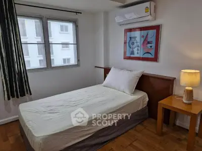 Cozy bedroom with single bed, modern art, and air conditioning in a well-lit apartment.