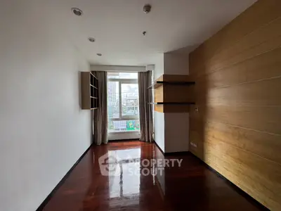 Spacious empty room with wooden floors and large window offering city view.