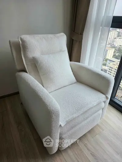 Cozy white armchair in a modern apartment with city view, perfect for relaxation.