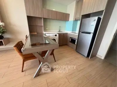 Modern kitchen with sleek cabinetry, glass dining table, and stainless steel appliances in a stylish apartment.