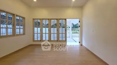 Spacious empty room with wooden flooring and large windows leading to a patio.