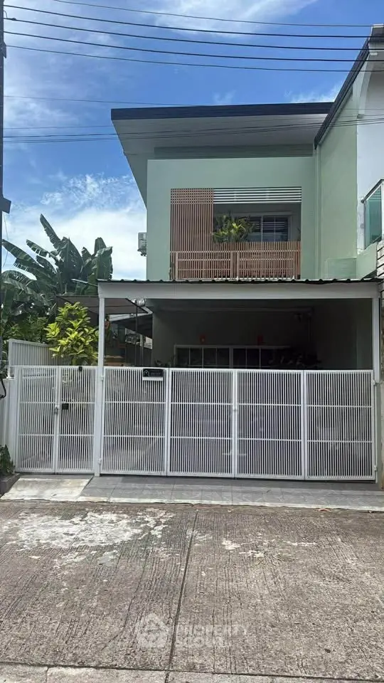 Modern two-story house with gated entrance and lush greenery, perfect for family living.