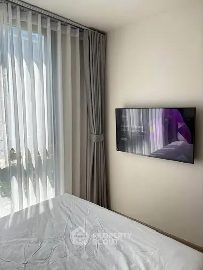 Modern bedroom with sleek TV and elegant curtains, showcasing minimalist design and natural light.