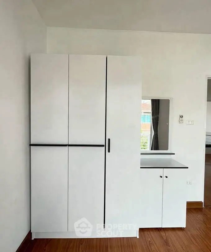 Modern minimalist bedroom with sleek white wardrobe and wooden flooring.