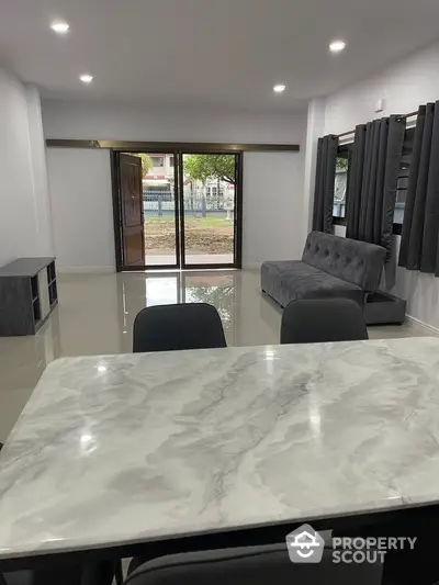 Modern living room with marble table and large windows overlooking garden.