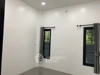 Minimalist room with white walls and two windows, featuring modern black frames and grey curtains.