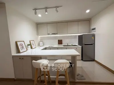 Modern kitchen with sleek design, featuring bar stools and stainless steel fridge, perfect for contemporary living.