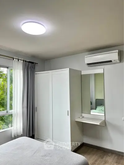 Modern bedroom with sleek wardrobe and air conditioning, featuring a large window with lush green view.
