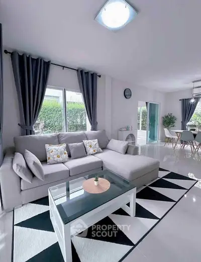 Modern living room with stylish decor, featuring a cozy gray sofa, glass coffee table, and elegant dining area.