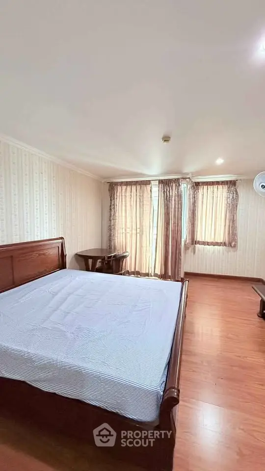 Spacious bedroom with wooden flooring and large windows for natural light.