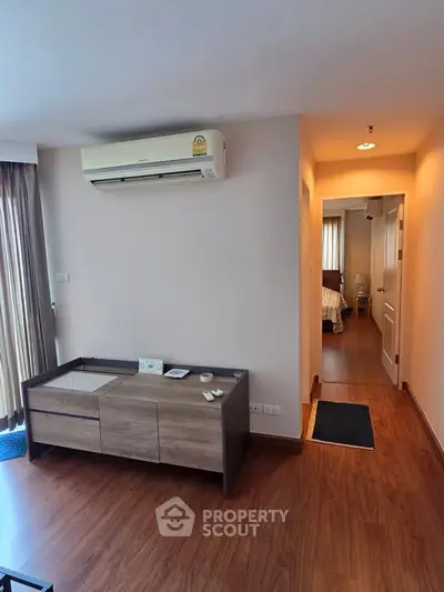 Modern apartment interior with wooden flooring and air conditioning, leading to a cozy bedroom.