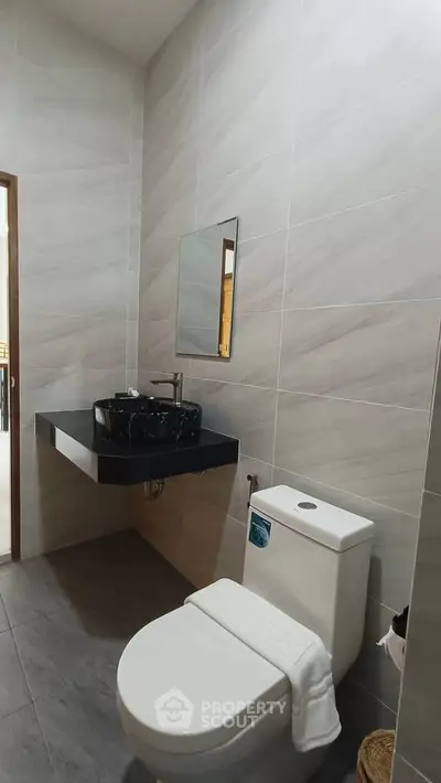 Modern bathroom with sleek black sink and white toilet in contemporary design.