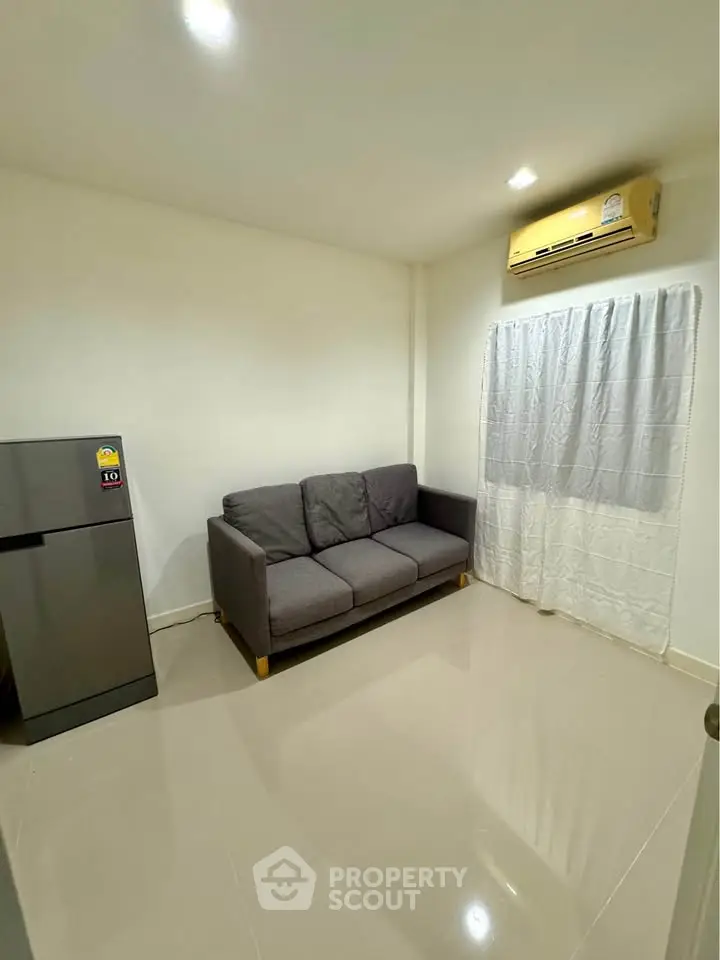 Cozy living room with modern sofa, air conditioning, and sleek refrigerator in a minimalist setting.