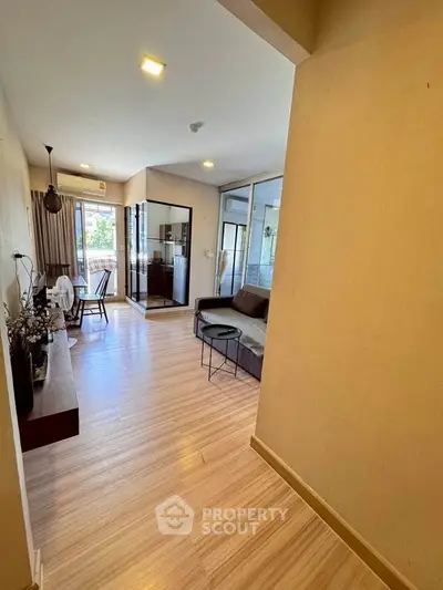 Modern living room with wooden flooring and glass partition, featuring cozy seating and natural light.