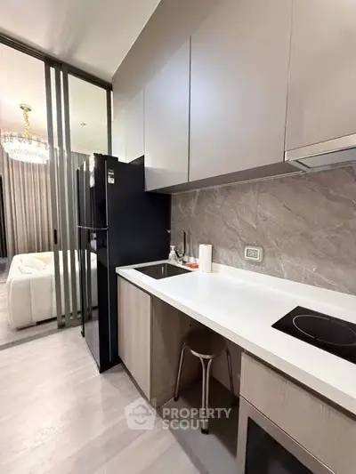 Modern kitchen with sleek cabinetry and open layout adjacent to living area, featuring elegant lighting.