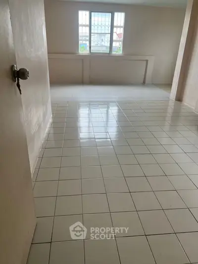 Spacious empty room with tiled flooring and large window, perfect for customization.