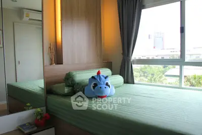 Cozy bedroom with green bedding and plush toy, featuring large window with city view.