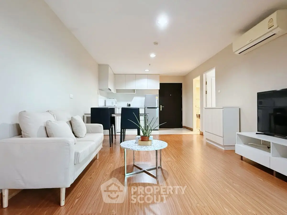 Modern open-plan living room with kitchen, featuring sleek furniture and wooden flooring.