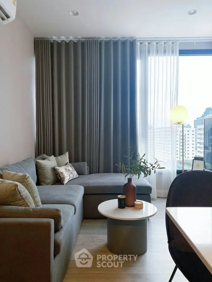 Modern living room with stylish gray sofa and city view through large window.