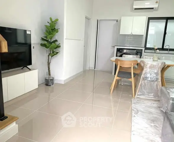 Modern open layout living room with kitchen, featuring sleek furniture and bright tiled flooring.