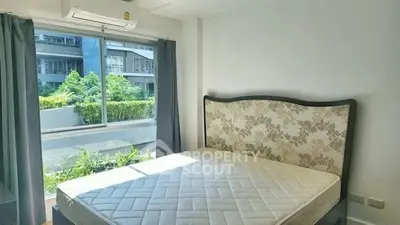 Bright bedroom with large window and elegant headboard, overlooking lush greenery.